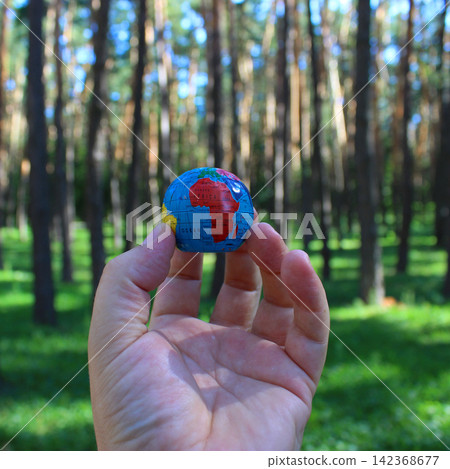 African continent on a small globe in a person's hand against a background of blurred green trees. Earth model in human hand environmental concept African continent on a small globe in a person's hand against a background of blurred green trees. Earth model in human hand environmental concept 142368677