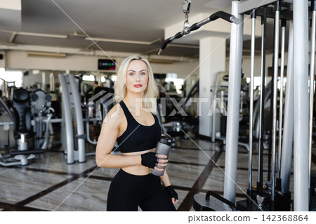 Determined sportswoman holding water bottle and training in gym Determined sportswoman holding water bottle and training in gym 142368864