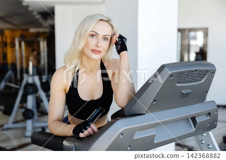 Determined sportswoman running on treadmill during fitness workout in gym Determined sportswoman running on treadmill during fitness workout in gym 142368882