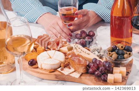 Sharing a platter of cheese, meats, olives, and grapes with drinks on a table during a social gathering Sharing a platter of cheese, meats, olives, and grapes with drinks on a table during a social gathering 142369013