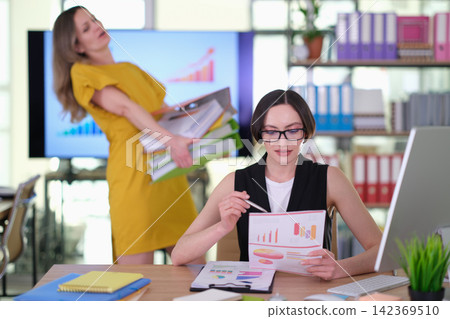 Businesswoman reviews report while coworker carries folders 142369510