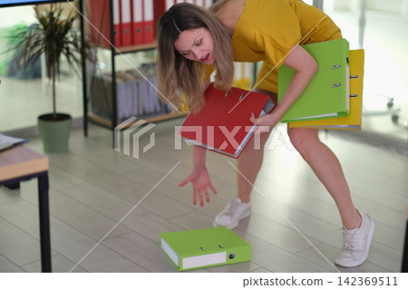 Overloaded businesswoman picks up fallen ring binder in office Overloaded businesswoman picks up fallen ring binder in office 142369511