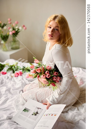 Female holding pink tulips while exploring garden catalog in cozy setting Female holding pink tulips while exploring garden catalog in cozy setting 142370088