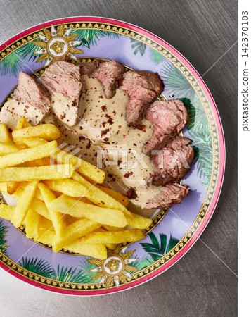 Sliced beef medallions with creamy pepper sauce on ornate purple and gold plate, fries on side, with beef, slice, tender, roastbeef detail, showing meat, sauce, cream, pepper context Sliced beef medallions with creamy pepper sauce on ornate purple and gold plate, fries on side, with beef, slice, tender, roastbeef detail, showing meat, sauce, cream, pepper context 142370103