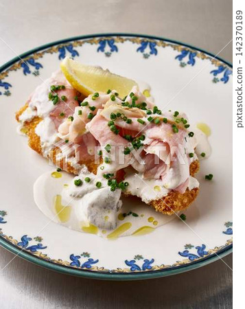 fried fish with cream sauce and garnish presented on a plate in a delicious and appetizing manner on a tabletop from a top-down viewpoint with white and brown colors. fried fish with cream sauce and garnish presented on a plate in a delicious and appetizing manner on a tabletop from a top-down viewpoint with white and brown colors. 142370189