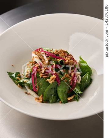 Fresh spinach salad with pickled red onion, white seafood rings, crispy fried shallots, and bright leafy garnish served in wide white bowl on metal table, with salad, spinach, onion, shallot detail Fresh spinach salad with pickled red onion, white seafood rings, crispy fried shallots, and bright leafy garnish served in wide white bowl on metal table, with salad, spinach, onion, shallot detail 142370190
