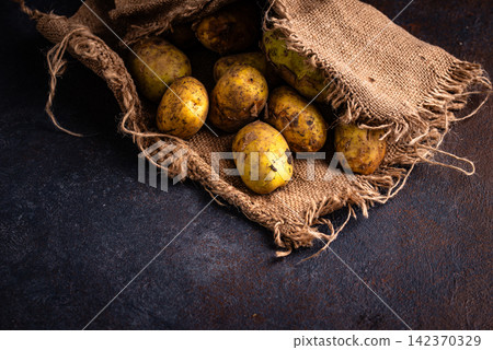 Raw uncooked potato on dark background Raw uncooked potato on dark background 142370329