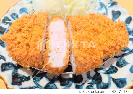 A photograph of a golden-brown pork cutlet served with shredded cabbage, showing the cross-section of the meat. A photograph of a golden-brown pork cutlet served with shredded cabbage, showing the cross-section of the meat. 142371174