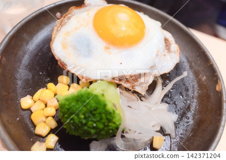 A close-up of a fragrant hamburger steak topped with a fried egg and colorful vegetables. A close-up of a fragrant hamburger steak topped with a fried egg and colorful vegetables. 142371204