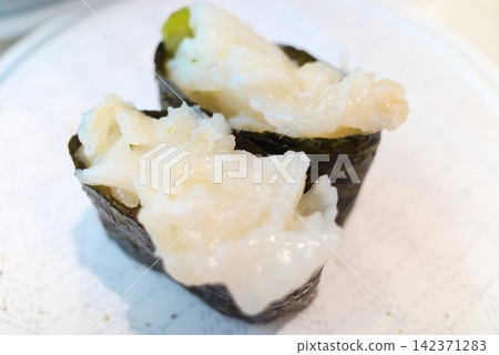 兩張軍艦壽司卷的特寫照片,上面鋪滿了白色的緣邊(比目魚鰭)。 兩張軍艦壽司卷的特寫照片,上面鋪滿了白色的緣邊(比目魚鰭)。 142371283