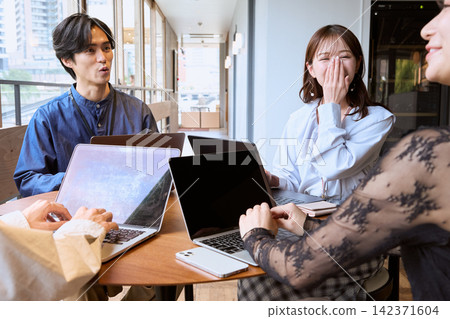 一群年輕男女在咖啡館裡一邊用筆記型電腦一邊聊天。 一群年輕男女在咖啡館裡一邊用筆記型電腦一邊聊天。 142371604