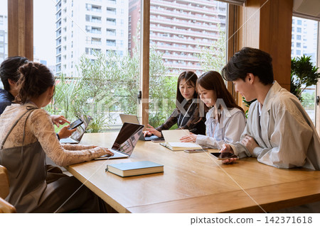 一支年輕的商務團隊在咖啡廳式的辦公室裡，使用筆記型電腦和平板電腦開會。 142371618