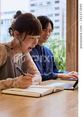 兩名年輕女子在咖啡館一邊使用筆記型電腦一邊聊天微笑。 142371640