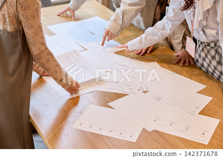 Businesswomen are having a meeting while reviewing documents spread out on the conference table. Businesswomen are having a meeting while reviewing documents spread out on the conference table. 142371678