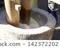 A traditional mochi-making process using a stone mortar and wooden pestle. 142372202