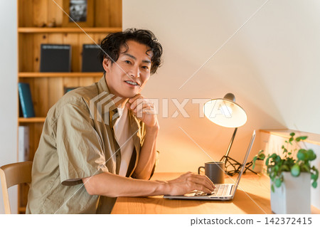 A middle-aged man working from home using a laptop computer. A middle-aged man working from home using a laptop computer. 142372415