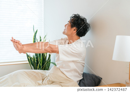 一位中年亞洲男子早上醒來，舒服地在床上伸了個懶腰。 142372487