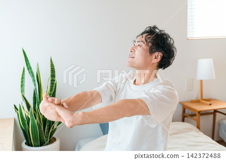 一位中年亞洲男子早上醒來，舒服地在床上伸了個懶腰。 142372488