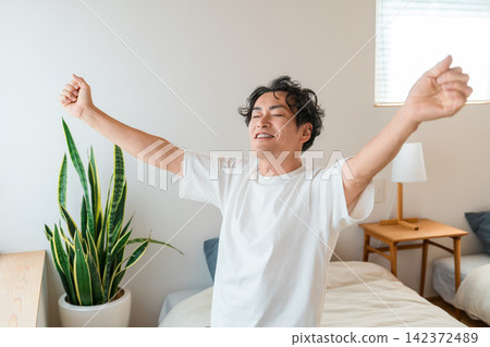 一位中年亞洲男子早上醒來,舒服地在床上伸了個懶腰。 一位中年亞洲男子早上醒來,舒服地在床上伸了個懶腰。 142372489