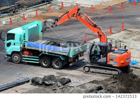 挖掘作業期間的挖土機和自卸卡車(用於傾倒土壤)。 挖掘作業期間的挖土機和自卸卡車(用於傾倒土壤)。 142372513