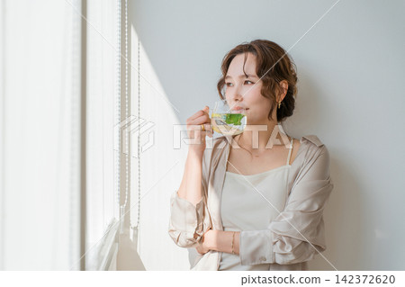 A woman relaxing by the window, enjoying herbal tea. A woman relaxing by the window, enjoying herbal tea. 142372620