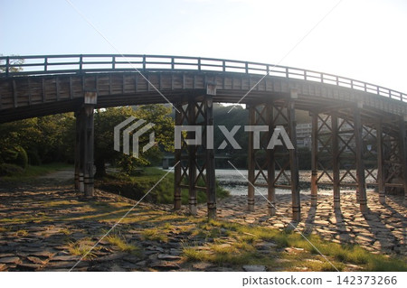 The Kintaikyo Bridge, a scenic spot spanning the clear waters of the Nishiki River in Iwakuni City, Yamaguchi Prefecture. A beautiful view of the wooden arch bridge bathed in the morning sun. The Kintaikyo Bridge, a scenic spot spanning the clear waters of the Nishiki River in Iwakuni City, Yamaguchi Prefecture. A beautiful view of the wooden arch bridge bathed in the morning sun. 142373266