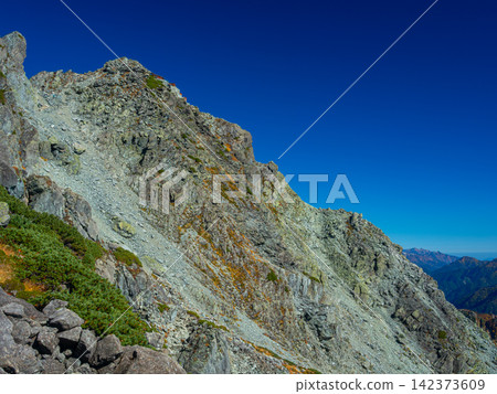 九月下旬,在晴朗的藍天下,北穗高山的崎嶇岩壁和北穗高山小屋矗立在山頂下方。 九月下旬,在晴朗的藍天下,北穗高山的崎嶇岩壁和北穗高山小屋矗立在山頂下方。 142373609