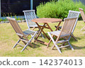 An outdoor rest area with a wooden table and folding chairs set up in a grassy garden. 142374013