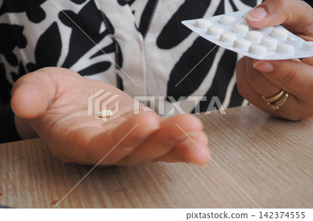 Person holding a pill in hand near a blister pack 142374555