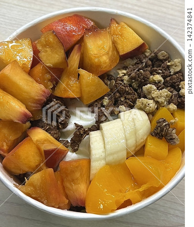 Swirled yogurt ice cream dessert served in a cup, smooth creamy texture with glossy surface, topped with fresh fruit pieces, highlighting its refreshing and inviting appearance in detail 142374841