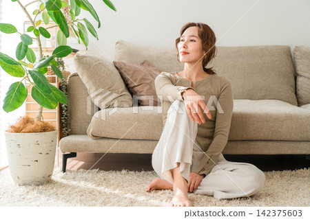 A woman enjoying a peaceful time in a bright living room. A woman enjoying a peaceful time in a bright living room. 142375603