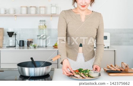 一位女士正在家裡的廚房準備一頓健康的餐點。 一位女士正在家裡的廚房準備一頓健康的餐點。 142375662