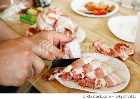 Man cutting fresh raw pork belly with knife on wooden board. Man cutting fresh raw pork belly with knife on wooden board. 142375915