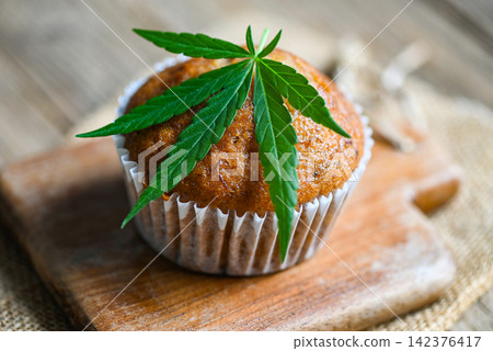 Cannabis food cake with cannabis leaf marijuana herb on wooden background, delicious sweet dessert cupcakes with hemp leaf plant THC CBD herbs food snack and medical concept Cannabis food cake with cannabis leaf marijuana herb on wooden background, delicious sweet dessert cupcakes with hemp leaf plant THC CBD herbs food snack and medical concept 142376417
