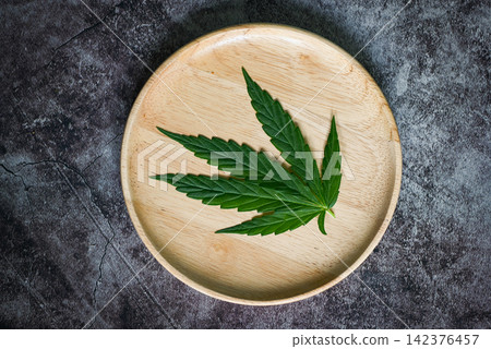 Cannabis leaf on wooden plate, marijuana leaves plant on dark background, cannabis food nature herb CBD THC concept Cannabis leaf on wooden plate, marijuana leaves plant on dark background, cannabis food nature herb CBD THC concept 142376457