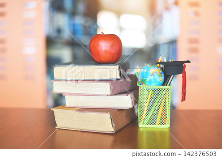 Books on the table in the library - Education learning old book stack and graduation cap on a pencil case with earth globe model on wood desk and blurred bookshelf room background with apple on book Books on the table in the library - Education learning old book stack and graduation cap on a pencil case with earth globe model on wood desk and blurred bookshelf room background with apple on book 142376503