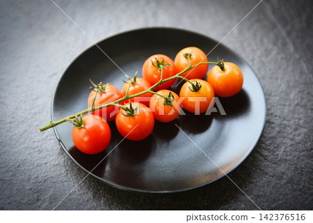 Ripe red tomato vine for cooked food on the table - Branch of fresh tomatoes on black plate with dark background Ripe red tomato vine for cooked food on the table - Branch of fresh tomatoes on black plate with dark background 142376516