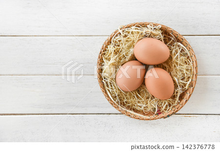 Chicken eggs in basket nest on white wooden background Chicken eggs in basket nest on white wooden background 142376778