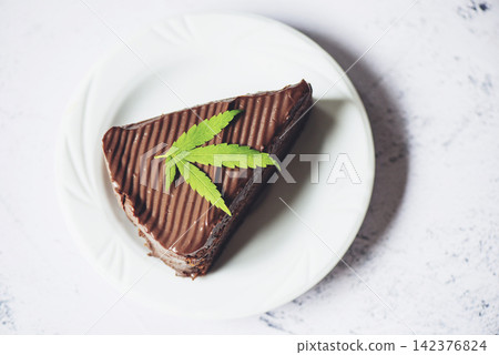 Chocolate cake with cannabis leaf - marijuana leaves plant on white plate, cannabis food nature herb Chocolate cake with cannabis leaf - marijuana leaves plant on white plate, cannabis food nature herb 142376824