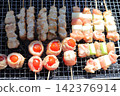 Grilling a mixed platter of yakitori on a net: chicken and green onion skewers and tomato skewers. 142376914