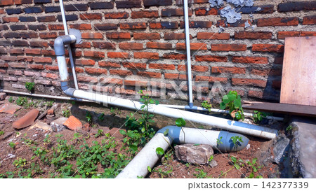Exterior PVC drainage pipe along a rustic red brick wall. Exterior PVC drainage pipe along a rustic red brick wall. 142377339