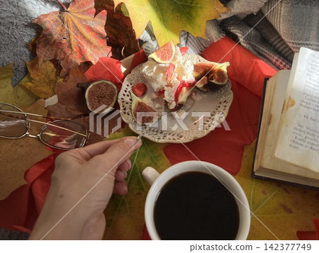 Cozy Autumn Flatlay with Female Hand Holding Fig, Coffee Cup, and Book Cozy Autumn Flatlay with Female Hand Holding Fig, Coffee Cup, and Book 142377749
