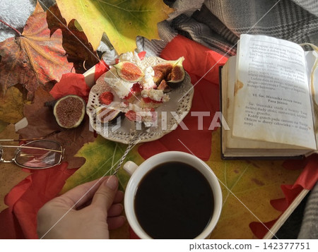 Cozy Autumn Flatlay with Female Hand Holding Fig, Coffee Cup, and Book Cozy Autumn Flatlay with Female Hand Holding Fig, Coffee Cup, and Book 142377751