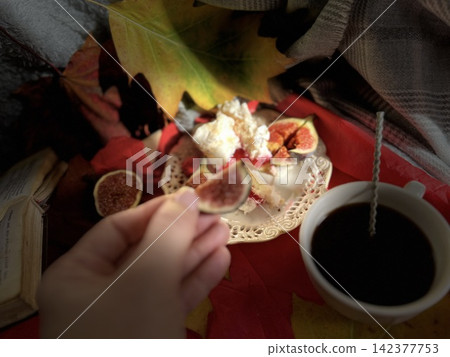 Cozy Autumn Flatlay with Female Hand Holding Fig, Coffee Cup, and Book Cozy Autumn Flatlay with Female Hand Holding Fig, Coffee Cup, and Book 142377753