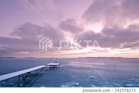 Frozen Lake with Snowy Pier Under Pink Winter Sunset Sky Frozen Lake with Snowy Pier Under Pink Winter Sunset Sky 142378273