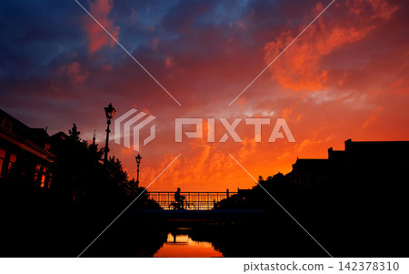 Sunset Sky Over Urban Canal with Cyclist Silhouette Sunset Sky Over Urban Canal with Cyclist Silhouette 142378310