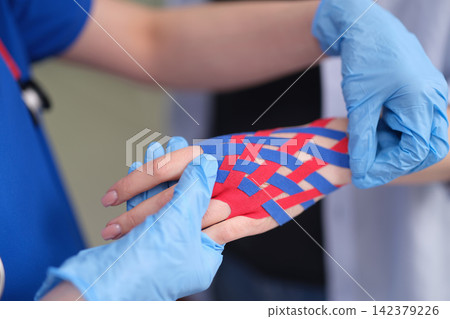 Doctor treating patient injured hand with kinesio tape closeup Doctor treating patient injured hand with kinesio tape closeup 142379226