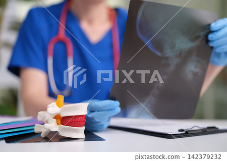 medical professional closely examines spine model in clinical office setting with stethoscope and gloves, focused and detailed close-up view of hands and objects. medical professional closely examines spine model in clinical office setting with stethoscope and gloves, focused and detailed close-up view of hands and objects. 142379232