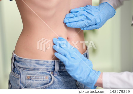 doctor examining patient's back in clinical setting with blue gloves and jeans over-the-shoulder perspective, professional healthcare interaction, skin tone, clean background, modern design. doctor examining patient's back in clinical setting with blue gloves and jeans over-the-shoulder perspective, professional healthcare interaction, skin tone, clean background, modern design. 142379239
