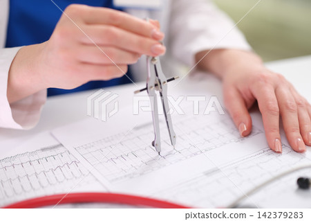 medical professional measuring heart rate in clinical environment with focused perspective and electrocardiogram paper on white and blue background. clean and professional setting. 142379283